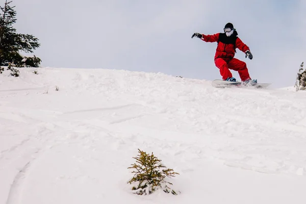 Парень в ярко-красном комбинезоне катается на сноуборде. — стоковое фото