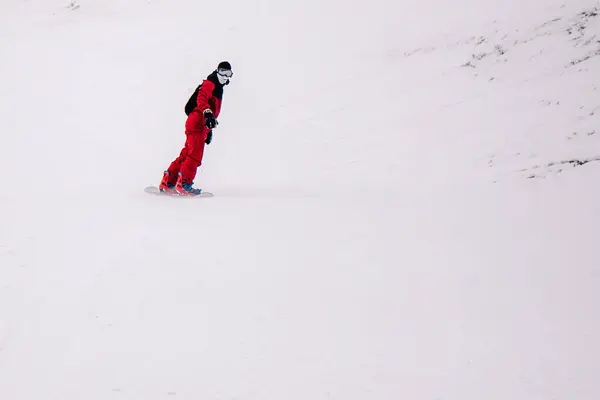 Ragazzo in tuta rossa brillante cavalca freeride su uno snowboard — Foto Stock