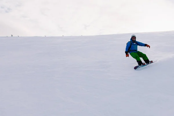 stock image Guy slides on a snowboard down the slope in a bright suit