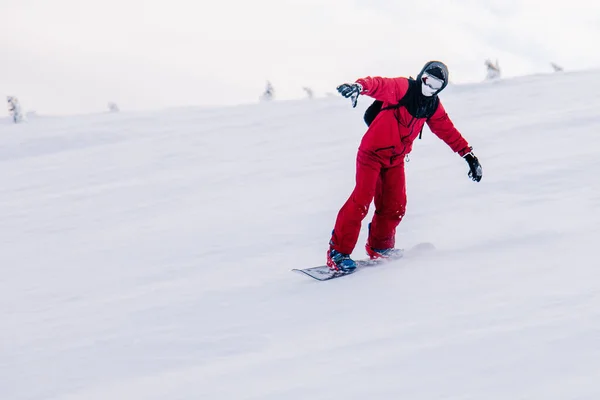 Chico se desliza por la pendiente en una tabla de snowboard en un mono rojo —  Fotos de Stock