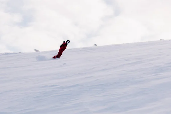 Chico se desliza por la pendiente en una tabla de snowboard en un mono rojo —  Fotos de Stock