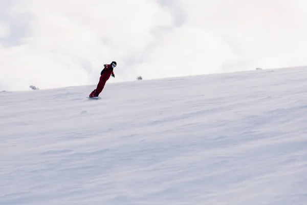 Le gars glisse sur la pente sur un snowboard en combinaison rouge — Photo