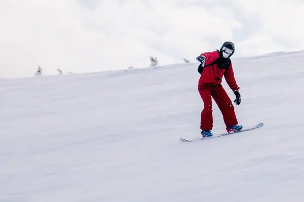 Killen glider nerför slänten på en snowboard i en röd overall — Stockfoto