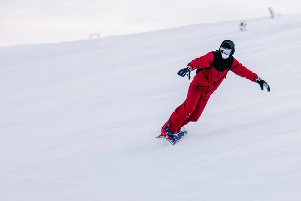 Парень скользит по склону на сноуборде в красном комбинезоне — стоковое фото