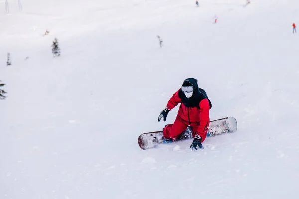 Парень летит вниз по схилу на сноуборді в красном костюме — стокове фото