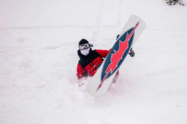 Парень в ярко-красном комбинезоне падает на сноуборд — стоковое фото