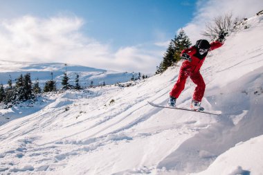 Kırmızı tulumlu bir adam snowboard 'a atlıyor.