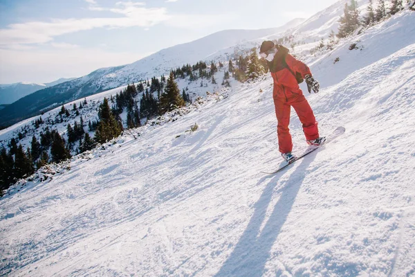 Guy gleitet im roten Jumpsuit auf einem Snowboard den Hang hinunter — Stockfoto