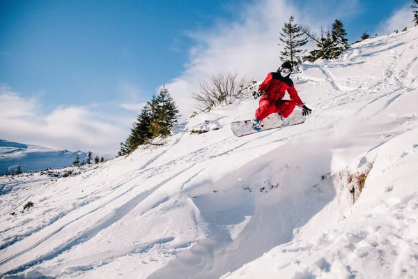 Facet w czerwonym kombinezonie skacze na snowboardzie. — Zdjęcie stockowe