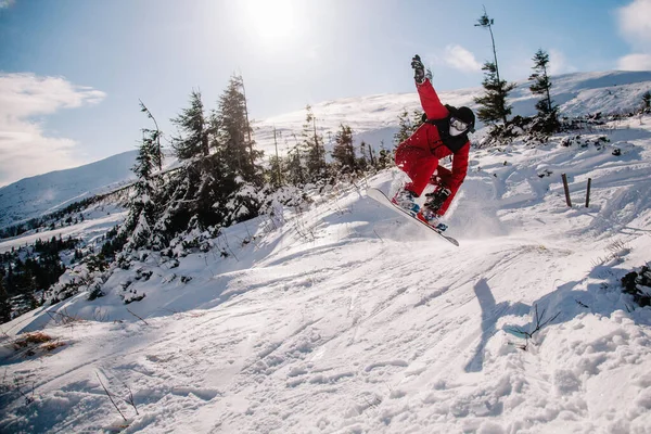 Facet w czerwonym kombinezonie skacze na snowboardzie. — Zdjęcie stockowe