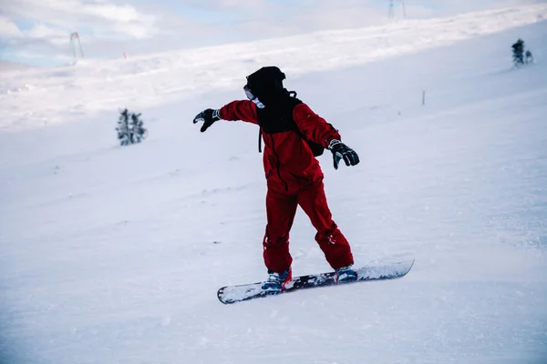 Guy scivola lungo il pendio su uno snowboard con una tuta rossa — Foto Stock