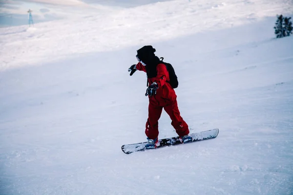 Guy glides down the slope on a snowboard in a red jumpsuit — Stock Photo, Image