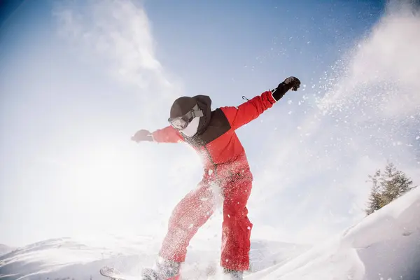 Парень в красном комбинезоне прыгает на сноуборде — стоковое фото