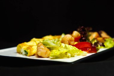 Siyah arka planda bir rulo omlet ve taze salata.