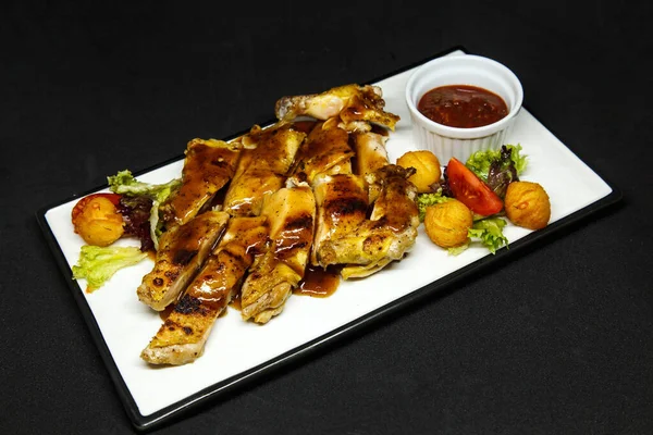 Pieces of grilled meat with sauce in a plate on a black background