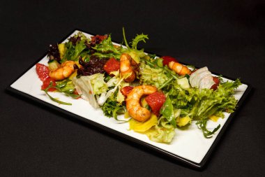 Dikdörtgen bir tabakta karides ve taze sebzeli salata.