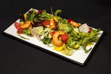 Dikdörtgen bir tabakta karides ve taze sebzeli salata.