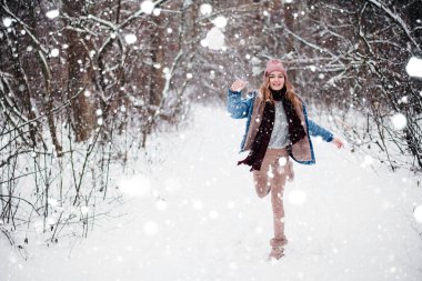 Genç, neşeli bir kız parka kartopu atar, kar yağar.