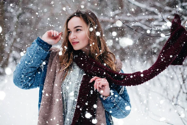 Young, beautiful girl with developing scarf stands in the park under snowfall — Stock Fotó