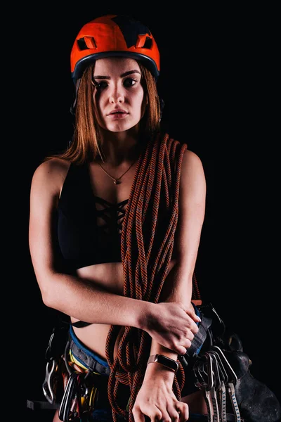 A girl in climbing gear poses against a black background