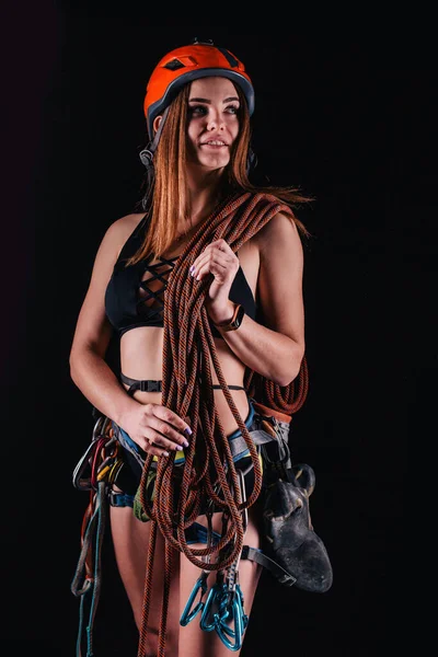 A girl in climbing gear poses against a black background