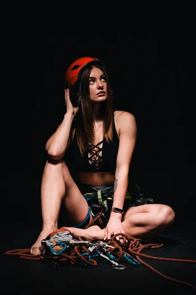 A girl in climbing gear poses against a black background