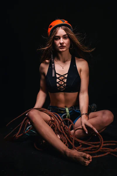 A girl in climbing gear poses against a black background