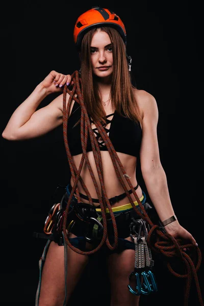 A girl in climbing gear poses against a black background