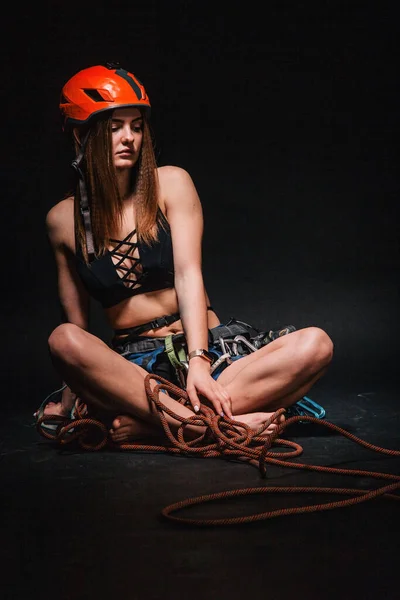 A girl in climbing gear poses against a black background