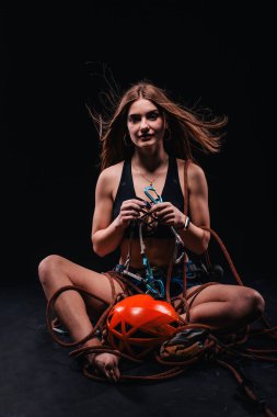 Dağcılık kıyafeti giymiş bir kız siyah bir arka plana karşı poz verir.