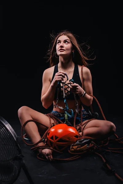 A girl in climbing gear poses against a black background