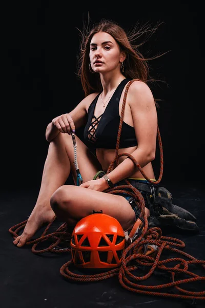 A girl in climbing gear poses against a black background