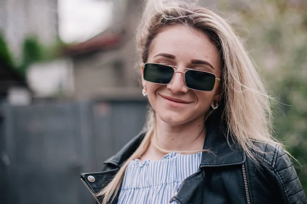 Young blonde in leather jacket and sunglasses posing in the street — Photo