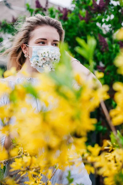 A girl in a medical mask decorated with live flowers poses in flowering trees — 스톡 사진