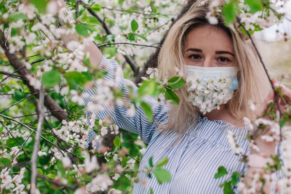 A girl in a medical mask decorated with live flowers poses in flowering trees — 스톡 사진