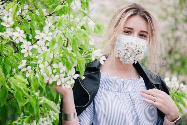 A girl in a medical mask decorated with live flowers poses in flowering trees — Fotografia de Stock
