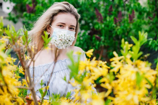 A girl in a medical mask decorated with live flowers poses in flowering trees — 스톡 사진