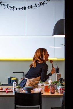 Cute housewife singing in the kitchen.Beautiful red hair young woman cooking and having fun at home,  in the kitchen.