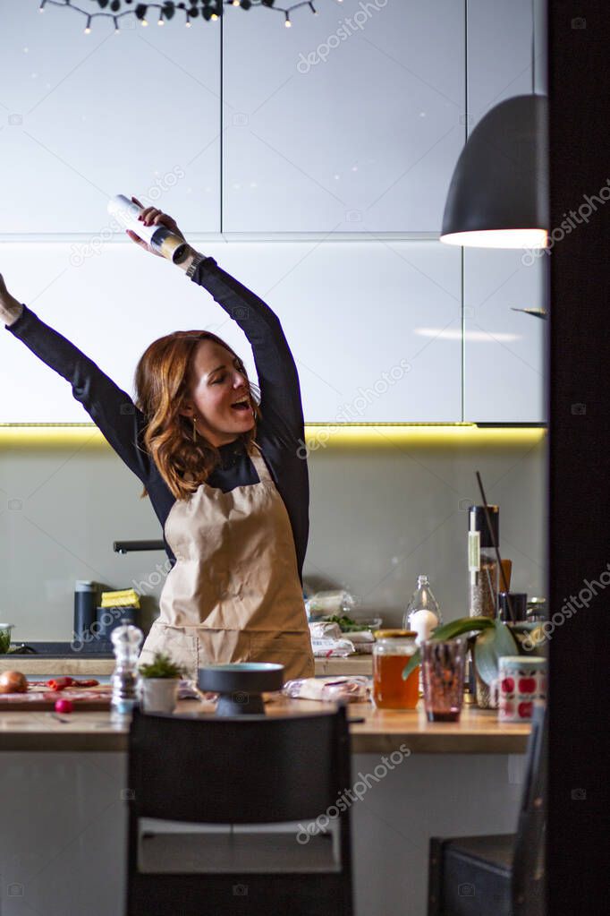 Cute housewife singing in the kitchen.Beautiful red hair young woman cooking and having fun at home,  in the kitchen.