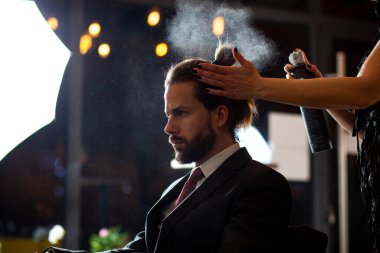 Uzun düz saçlı güzel adamlara yakın. Saç stilisti, bir güzellik salonunda genç ve yakışıklı işadamına saç tarıyor ve kurutuyor..