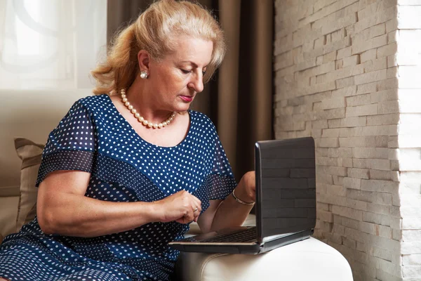 Mulher sênior com laptop na sala de estar — Fotografia de Stock