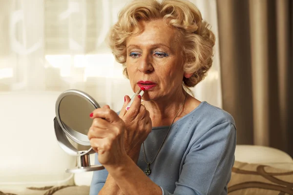 Elderly woman applied lipstick and looked in the mirror — Stock Photo, Image