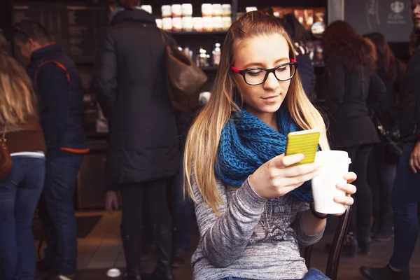 Young blonde girl drinking coffee and texting message in cafe. — Stock Photo, Image