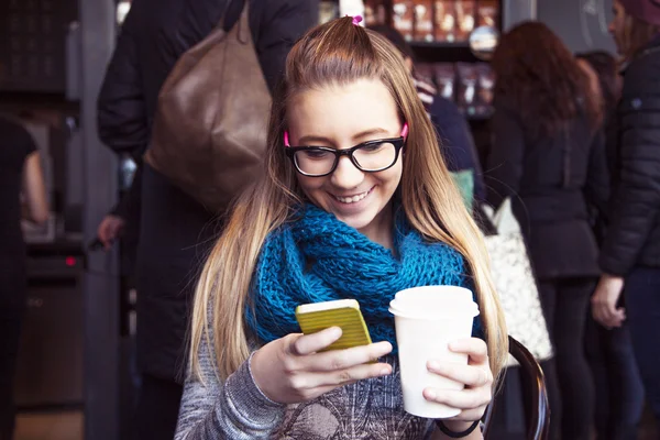 Mladá blondýnka pití kávy a textových zpráv v kavárně. — Stock fotografie