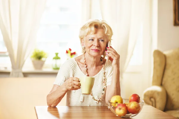 Blonde eldery woman using cell phone, at home — Stock Photo, Image