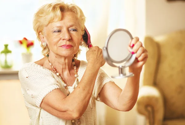 Lächelnde ältere Frau kämmte die Haare und blickte in den Spiegel — Stockfoto