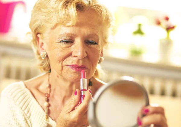 Elderly woman applied lipstick and looked in the mirror — Stock Photo, Image