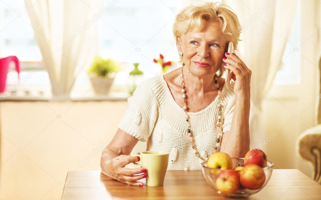 Blonde eldery woman using cell phone, at home