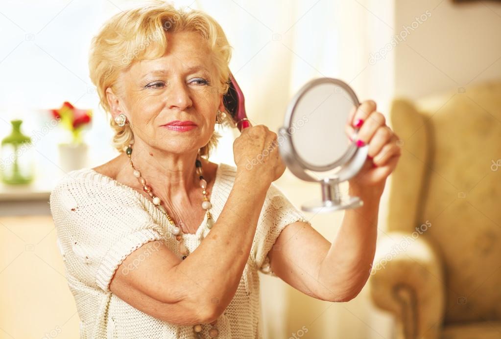 Smiling elderly woman comb hair and looked in the mirror