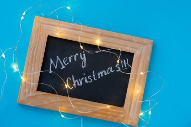 Tahta çerçeve, siyah karatahta ve yazılı kelimeler Mutlu Noeller ve etrafına bukleli çelenkler